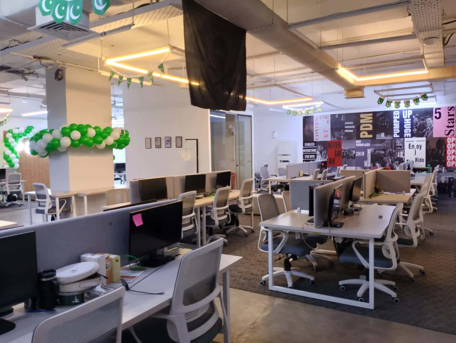 A large open-plan RSpace office floor with rows of white desks, monitors and warm linear lighting