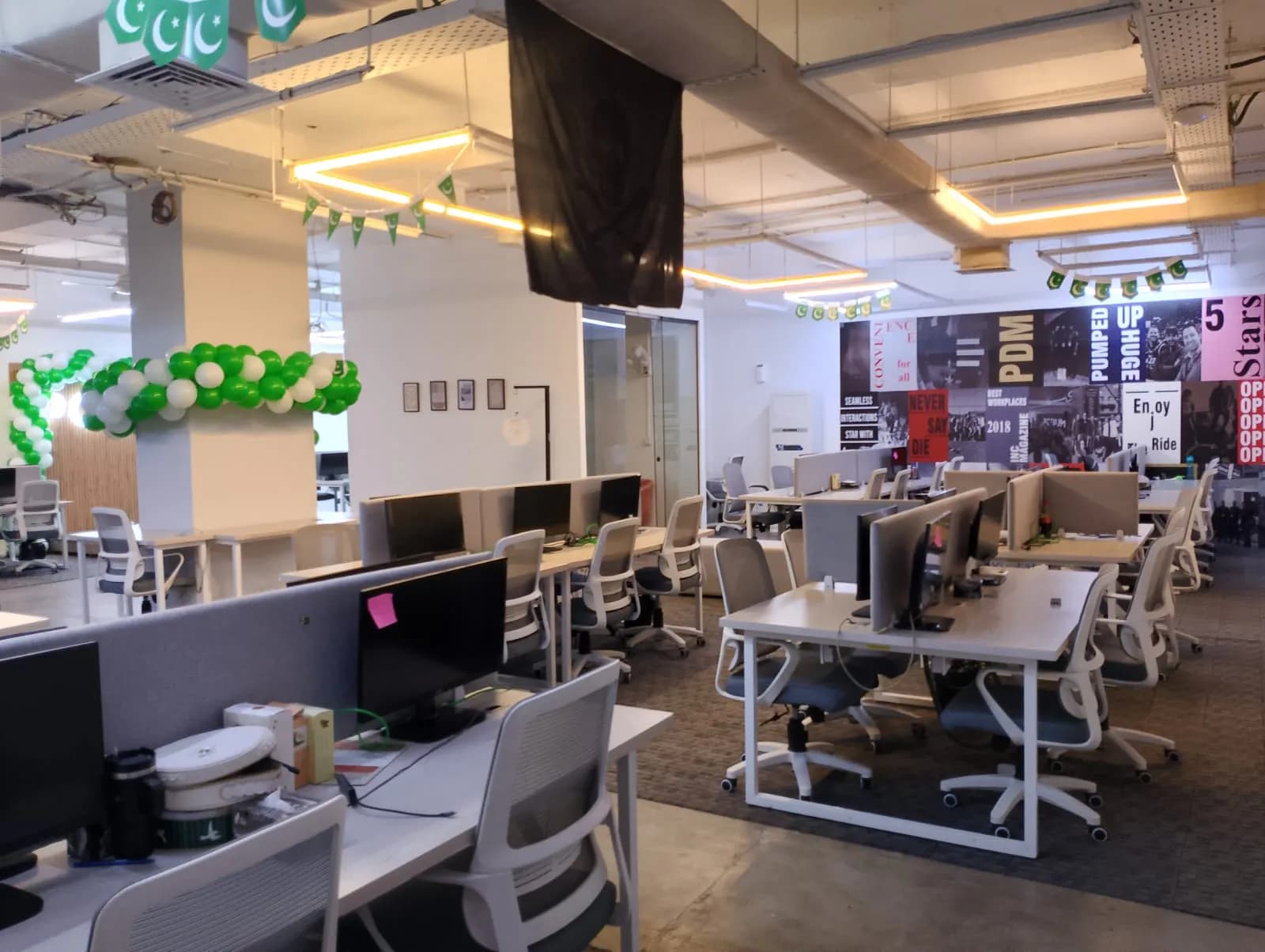 A large open-plan RSpace office floor with rows of white desks, monitors and warm linear lighting
