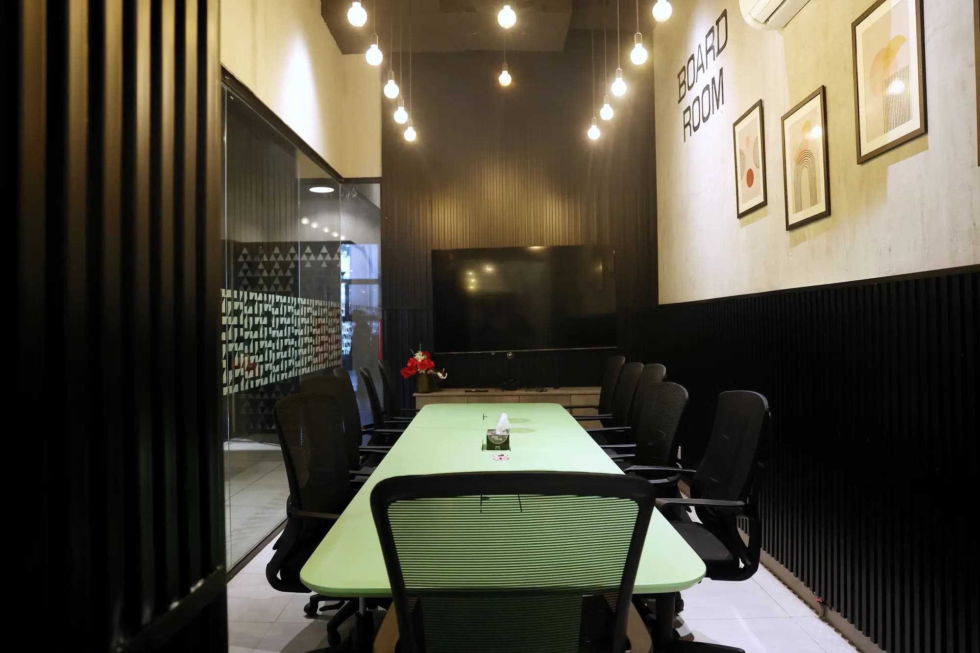 The boardroom and meeting room at RSpace Gulmohar Trade Centre, with a long green table, framed art and pendant lights